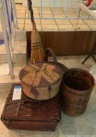 Woven basket set including a large rectangular basket, cylindrical basket, and a round lidded basket with a witches broom placed behind the baskets.