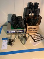 Three sets of binoculars with boxes, magnifying glass with adjustable arm and clamps, and a black tool holder with a spatula-like tool.