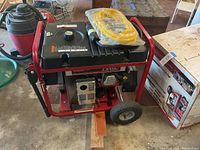 Front side of generator showing black fuel tank, red frame, wheels and yellow extension cord on top