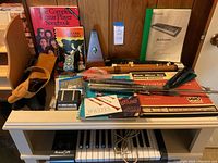 A table with music books, soprano recorders, a mechanical metronome, and music accessories such as cables and a small box.