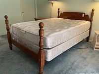 Queen-size wooden bed shown from side angle with mattress and box spring on blue carpet.
