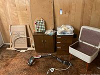 View of entire sewing area including sewing cabinet, thread holder with spools, smaller cabinet with drawers, cork board, and storage bench.