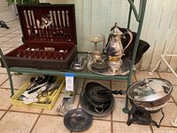 Wide view of silver plated flatware set in wooden case, silver plated tea set, trays and servers on glass shelf and floor