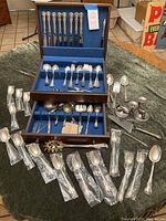 Overall lot overview showing wooden chest, flatware pieces, bagged utensils and candlesticks