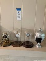Full suite of items on shelf including anniversary clock, two pocket watches under domes, silver urn