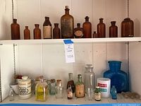 Overview of two shelves containing a variety of vintage glass bottles, both amber and clear, along with ceramic and plastic containers.