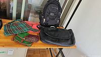 Full view of the lot on wooden table showing black leather computer bag, black backpack and four ladies purses in various colors including vintage