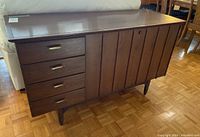 Front angle view of cedar chest showing four drawers on left side and door on right side with vertical wood paneling, resting on tapered legs.