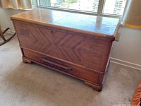 Front and top view of cedar chest showing wood veneer pattern and damage on top surface.