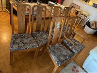 Six wood dining chairs and one captain's armchair with floral upholstered seats grouped near a dining table.
