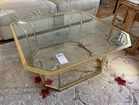 Top-down view of octagonal coffee table showing beveled glass top and metal base on floral carpet.