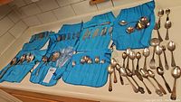 Wide view of cutlery laid out including forks, spoons and knives in a blue cloth organizer on counter.