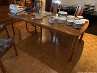 Full view of rectangular wood dining table set up with various household items on top. Shows overall condition, size and style.
