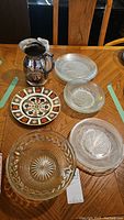 Overview of the lot showing the Royal Crown Derby plate, stainless steel jug, and assorted clear glass bowls and plates on a wooden table.