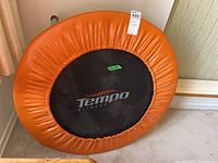 Full view of the trampoline showing the orange padded edge and black jumping mat with Tempo Fitness branding.
