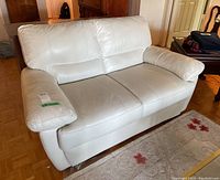 Full view of white faux leather loveseat showing front and side with cushioned armrests and visible affixed seat and back cushions.