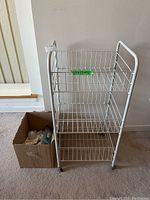 Front view of white metal utility cart with a green size label and box of assorted lightbulbs beside it on carpet