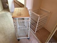 Photo showing both metal wire utility carts side by side, one with wood top and wheels, other with multiple drawers but no top.