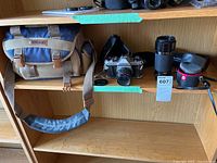 Two-shelf wood display; Nikon bag on left, Pentax K1000 center, telephoto lens and cases right