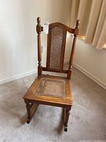 Front angle view of the vintage wooden rocking chair showing cane seat and back with carved posts and finials.
