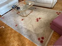 Full view of the large beige area rug laid out on wooden parquet flooring under glass coffee table and near white and purple sofa seating.