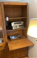 Sklar-Peppler wooden bookshelf with two electronic devices on the middle shelf and a silver item on the drop-down front shelf, partially open.