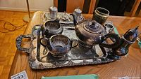 Full view of silver plated tea set on large serving tray showing teapot, cream, sugar, tea strainer, condiment dishes, brass vase, and shaker
