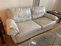 Full view of faux leather sofa showing two cushions, padded armrests, and light wear spots, fits contemporary style interior.