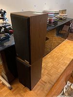 Two Paradigm speakers stacked, showing wood veneer side and grille front.