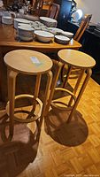 Two identical wooden stools with circular seats and four legs, seen from above and slightly side angles.