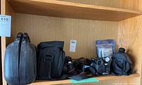 Three video cameras with their carrying cases on a wooden shelf.