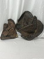 Two abstract textured sculptures placed side by side on plain white backdrop, showing their dark brown and black earthy colors and organic shapes.