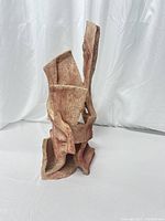 Front angle view of the clay abstract tower sculpture showing its twisting and flowing form with natural clay texture and earthy tones.