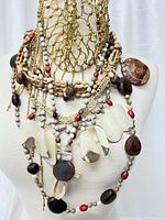 Photo of multiple large exotic bead statement necklaces draped on a mannequin bust, featuring natural wood, coral-colored, cream, and white carved elements.