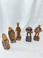 Front view of five hand carved wooden folk art villager figurines arranged side by side on white cloth background.