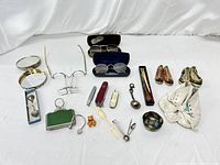 Wide view of assembled lot showing vintage eyeglasses, sewing kits, miniature shoes and various trinkets on white cloth background.