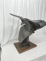 Front-left side view of the black metal abstract sculpture showing dynamic curves and sharp edges on the wood base.