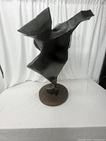 Front view of black metal abstract sculpture on round wooden base, showing contour and texture details.