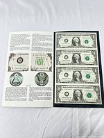 Uncut sheet of four one dollar bills along with an informational booklet showing detailed notes on serial numbers and seals.