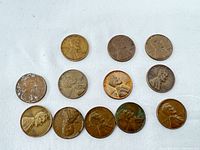 Top-down view of 12 US Wheat pennies showing obverse side with Lincoln profile, varying wear and discoloration.
