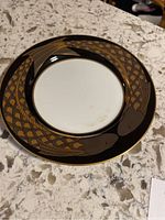 Flying fish design on black and gold porcelain dinner plate featuring two stylized fish circling the rim.