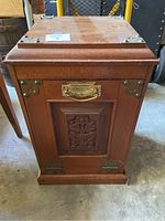 Front view showing carved wood panel and metal handle with accents on the corners of the coal bin.
