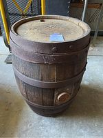 Full view of old wooden barrel showing weathered wood and metal bands, along with spigot on side.