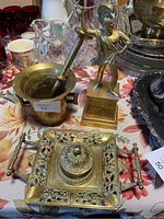 Photo showing heavy brass mortar and pestle, brass Greek statue, and ornate brass ink well on floral tablecloth.
