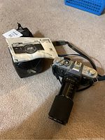 Photo of Canon FTb camera with telephoto lens, instruction manual, and carrying case on carpeted floor.