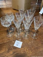 Photo showing seven champagne flutes and two wine glasses on hardwood floor, all with clear detailed cross and olive cut pattern. Two champagne flutes have visible chips.