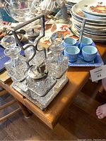 Photo showing silver and crystal condiment holder caddy with four cut-glass containers and faceted stoppers, placed on a wooden table