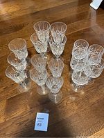 Wide view of 14 assorted crystal stemware glasses arranged on wooden floor, showing varied sizes and designs with cross and olive pattern etched on glass.