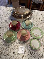Set of four colored demi tea cups with matching saucers, two small china plates, and silver serving tray on marble countertop