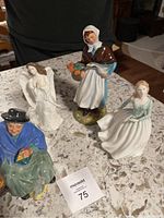 Four assorted Doulton figurines shown together on a table: elderly woman feeding birds, praying angel, woman in bonnet with basket of flowers, seated woman in green dress.